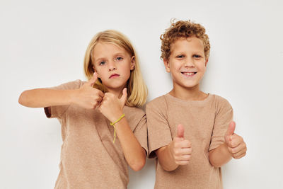 Portrait of boy and girl showing thumbs up gesture against white background