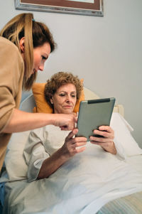 Young woman using mobile phone while sitting on bed at home