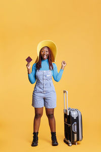 Portrait of young woman wearing hat standing against yellow background