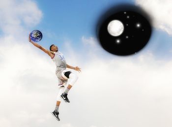 Low angle view of man jumping ball against sky