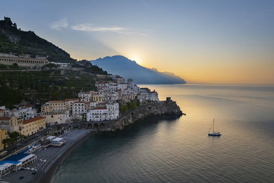 Sea with nautical vessel near town at sunrise