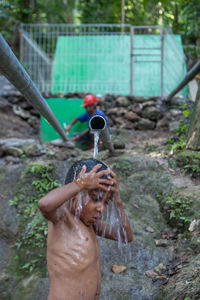 Shirtless boy standing under falling water from pipe