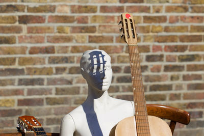 Mannequin with guitar on sunny day against brick wall