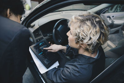 Female mechanic explaining customer over digital tablet while sitting in car
