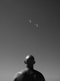 Rear view of bald man looking at bubbles against sky