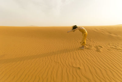 Woman in yellow dress playing with the wind in the desert