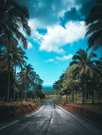 Road amidst palm trees against sky