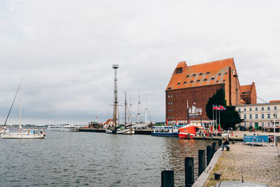 Sailboats in river by buildings in city against sky