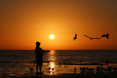 Silhouette woman standing at beach against sky during sunset