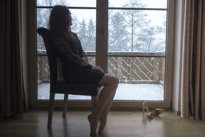 Young woman sitting by window at home during snowfall