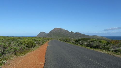 Road amidst green landscape against clear blue sky