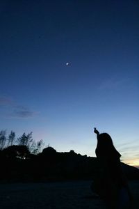 Silhouette man sitting against blue sky at dusk