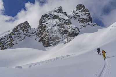 Rear view of people skiing on snowcapped mountains against sky