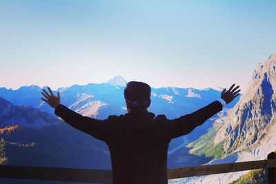 Rear view of man standing on snowcapped mountain against clear sky