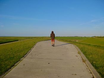 Rear view of woman walking on road amidst field against sky