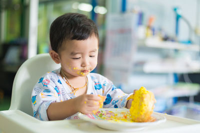 Boy with messy face sitting by food in plate on table