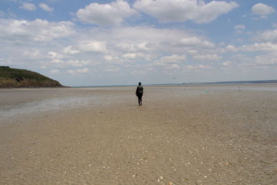 Rear view full length of woman walking at beach against sky