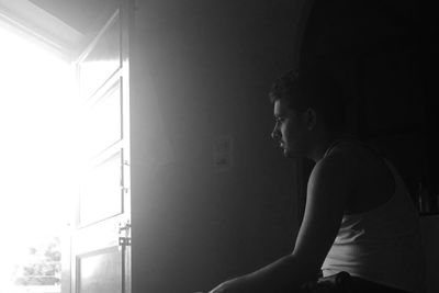 Sad man sitting in front of open door in darkroom