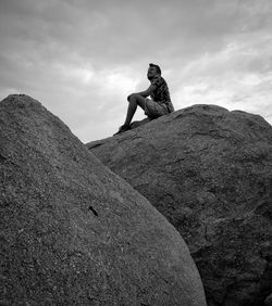 Low angle view of man sitting on rock against sky