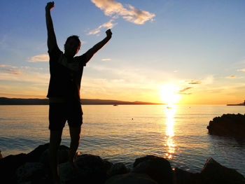 Man standing on rocks at sea shore against sky during sunset