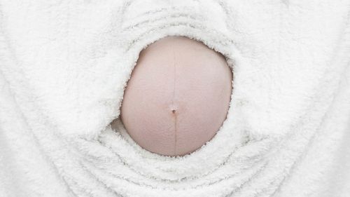 Cropped image of pregnant woman abdomen amidst white towel