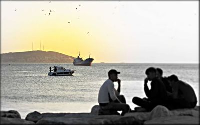 Rear view of people sitting on beach at sunset