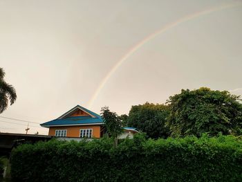 Rainbow over building and trees against sky