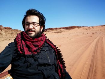 Man sitting in vehicle on sand against clear blue sky at desert