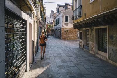 Rear view of woman walking on footpath amidst buildings in city