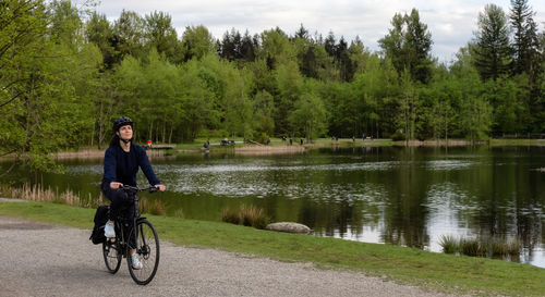 Man riding bicycle by lake against trees