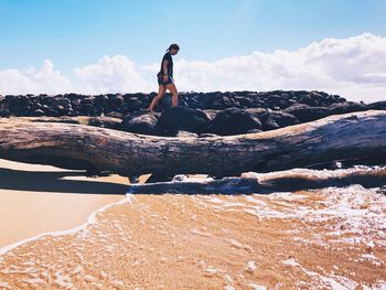 Full length of young woman on rock at beach against sky