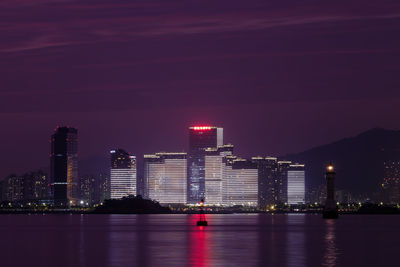 Illuminated city by river against sky at night