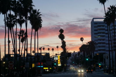 Silhouette city street against sky during sunset