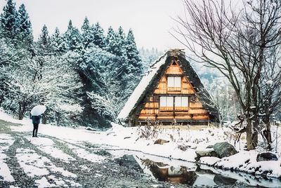 Snow covered trees by houses on field during winter