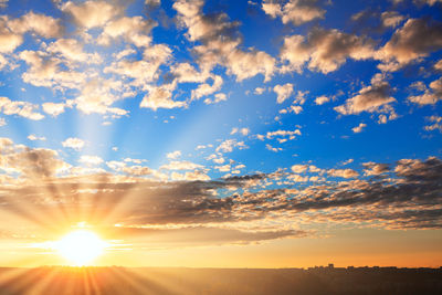 Low angle view of sunlight streaming through clouds during sunset