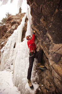 Full length of hiker climbing frozen waterfall