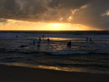 Silhouette people enjoying at beach against cloudy sky during sunset