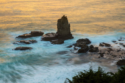 Rock formation in sea against sky at sunset