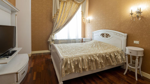 A bedroom in yellow tones with large bed and tv in front of it.