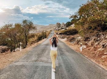 Rear view of woman on road amidst trees against sky
