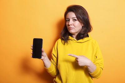 Young woman using mobile phone against yellow background