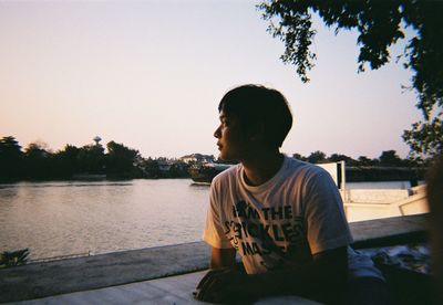 Man looking away while sitting by lake against sky