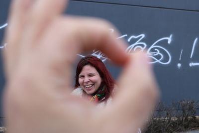 Portrait of cheerful woman seen through human hand sign outdoors