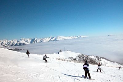 People skiing on snowcapped mountain against clear sky