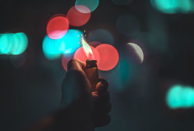 Close-up of human hand holding illuminated cigarette lighter against illuminated lights