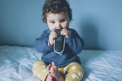 Cute girl biting shoe while sitting on bed at home