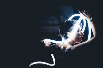 Mid adult woman holding illuminated fiber optic cable in darkroom