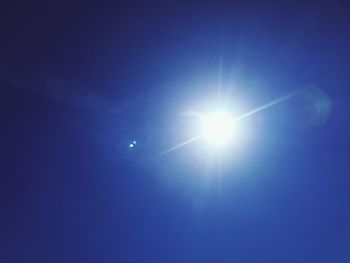 Low angle view of bright sun against blue sky