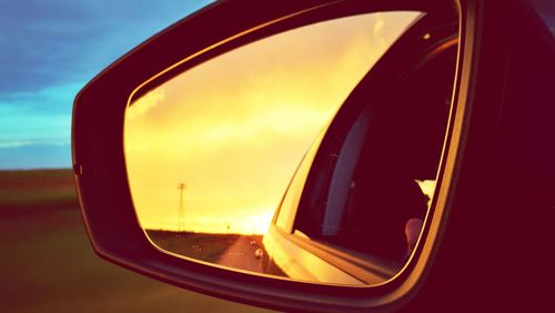 Close-up of side-view mirror against sky