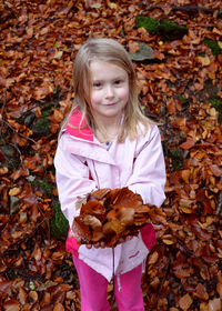 Portrait of girl holding dry leaves on field